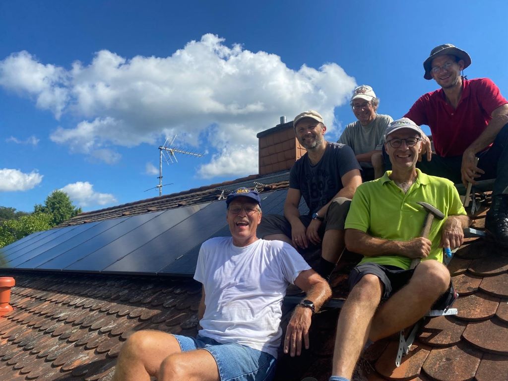 Mitglieder der Selbstbaugruppe sitzen auf einem Dach mit PV-Modulen